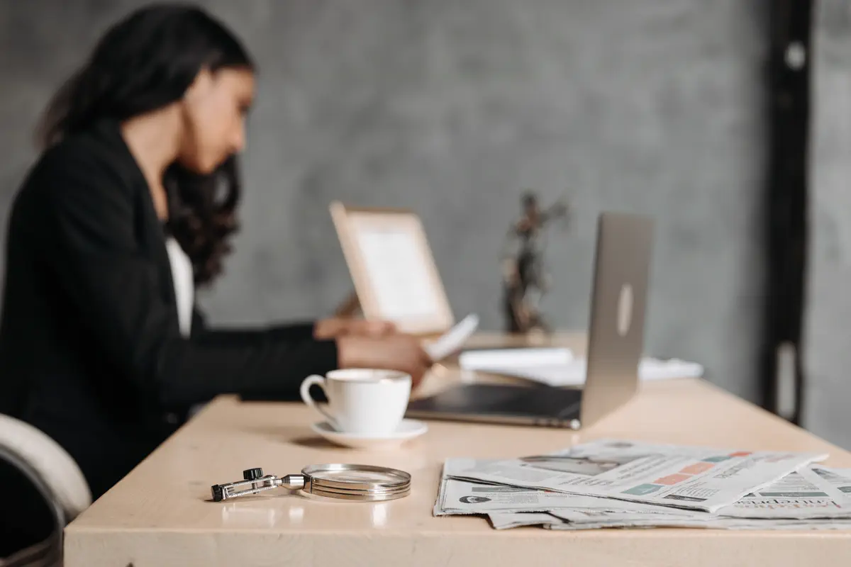 Woman reviewing papers at a desk beside a laptop and magnifying glass