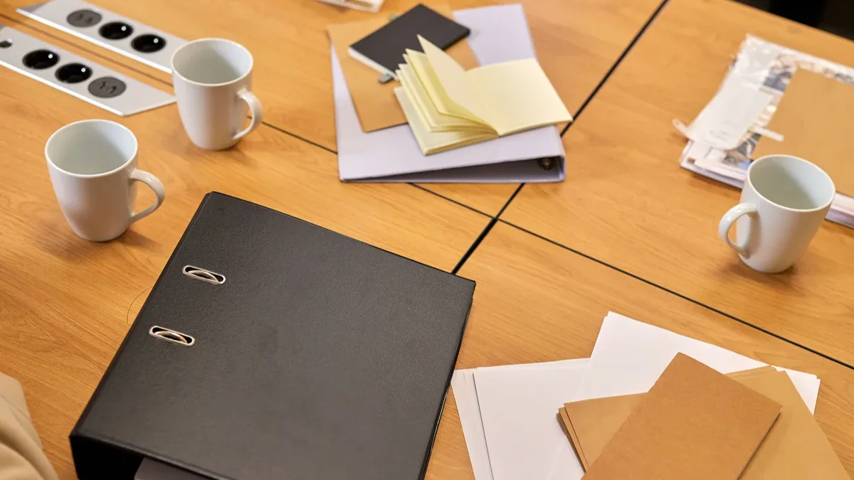 Office table with a binder, papers, notebooks, and mugs