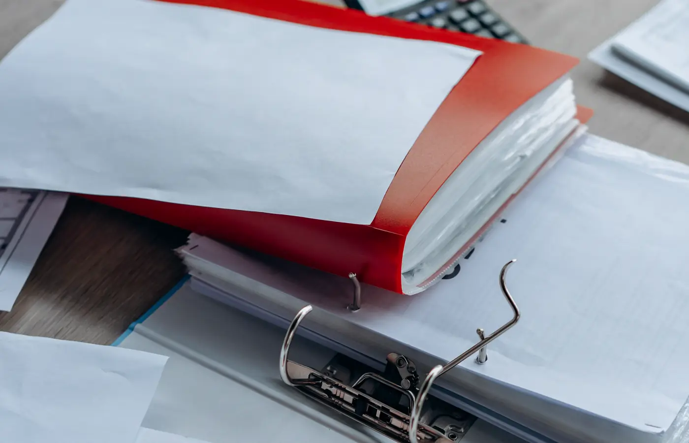 Open red and grey binders with stacked paperwork on an office desk